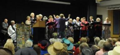 Choir singing with Elizabeth conducting and Chris Hedges accompanying